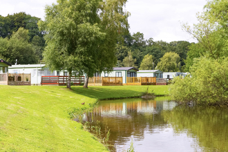 Image of a row of static caravans in a leisure park, surrounded by trees, next to a body of water.