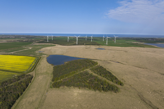A photo of West Chevington, featuring a mixture of fields, woodland, ponds and wind turbines. In the background can be seen Druridge Bay and the sea.