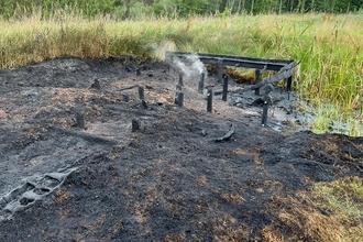 Image shows the burnt remains of the boardwalk and dipping platforms at East Chevington Nature Reserve, still smoking from the fire. Most structure has been completely burnt to ash.
