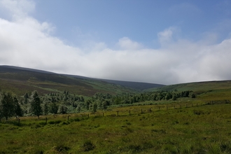 Green rolling hills for miles into the distance. The sky is blue with large clouds in the far distance.