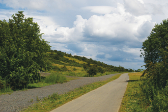 A path running between a grassy hill and field.
