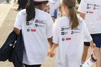 Two children wearing white t-shirts with project logos holding hands back to camera