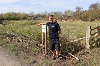 Callum Connelly, NWT Project Assistant standing next to the new hawthorn hedge with a field in the background. Image by Fiona Dryden.