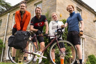 Four members of the HandleBards standing behind a bicycle in front of a building. Image by The Handlebards.