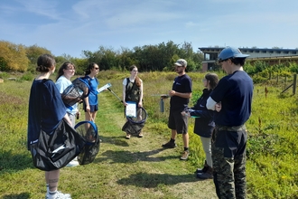 A small group of young people standing in a sunny meadow learning how to survey for butterflies.