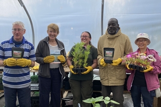 Five winners wearing gardening gloves standing in a row, holding pots of flowers. Image by NWT.