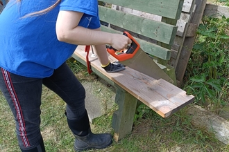 Raven is seen to be holding a saw in her right hand as it is placed onto the wood ready for sawing action.  