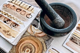 Abstract art on textured paper in earthy tones, alongside a stone mortar and pestle used for natural pigments.