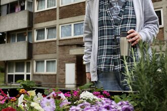 Man standing admiring flowers in front of a block of flats. Image by Abbey Wilkinson.