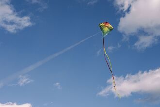 A colorful kite with long streamers flying high in a blue sky with scattered clouds.