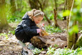 Young girl in the woods, crouching with a magnifying glass.