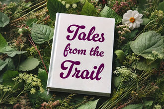 Book titled “Tales from the Trail” lying on a bed of green leaves and wild plants outdoors.