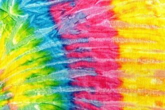 Close-up of brightly colored tie-dye fabric with blended bands of green, blue, pink, orange, and yellow in a soft, textured pattern.