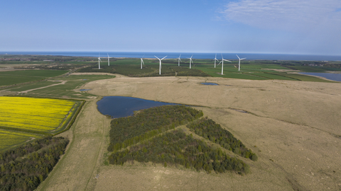 A photo of West Chevington, featuring a mixture of fields, woodland, ponds and wind turbines. In the background can be seen Druridge Bay and the sea.
