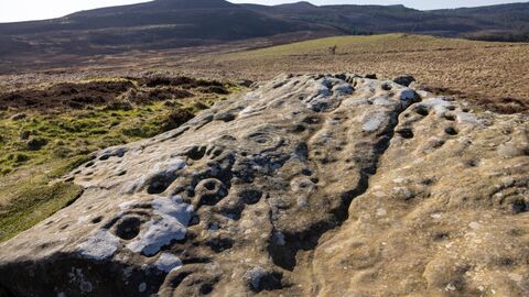 An ancient rock carving. Hollows and grooves known as cup and ring marks can be seen on a large swathe of stone
