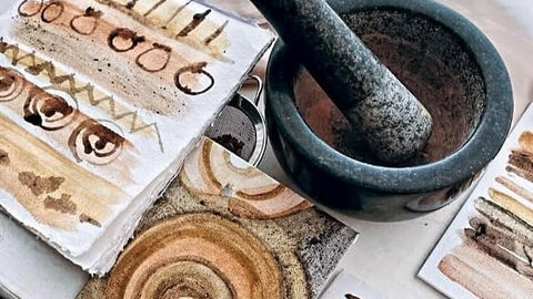Abstract art on textured paper in earthy tones, alongside a stone mortar and pestle used for natural pigments.