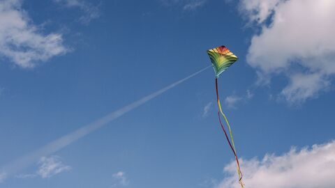 A colorful kite with long streamers flying high in a blue sky with scattered clouds.