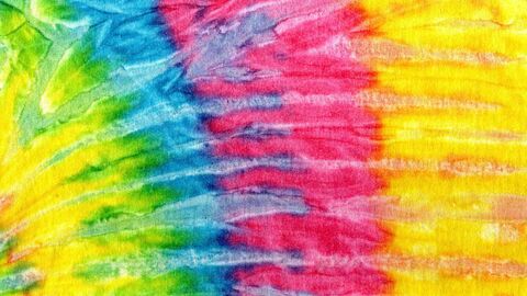 Close-up of brightly colored tie-dye fabric with blended bands of green, blue, pink, orange, and yellow in a soft, textured pattern.