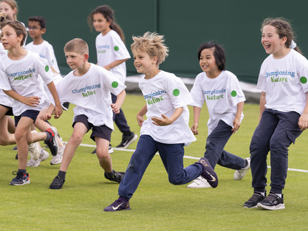 Smiling children on a tennis court in white Championing Nature t-shirts