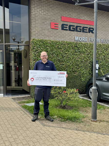 Graham Holyoak (NWT) standing in front of Egger UK building with a large cheque. Image by Egger Hexham.