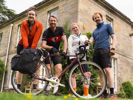 Four members of the HandleBards standing behind a bicycle in front of a building. Image by The Handlebards.