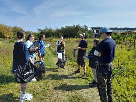 A small group of young people standing in a sunny meadow learning how to survey for butterflies.