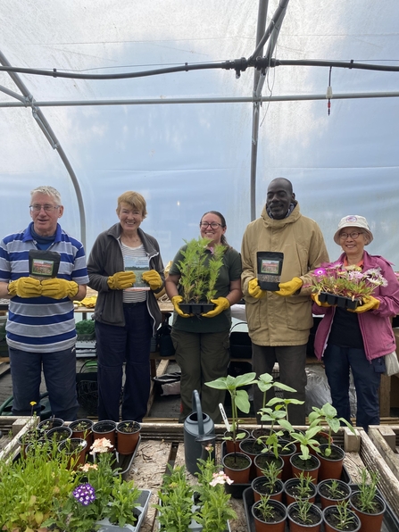 Five winners wearing gardening gloves standing in a row, holding pots of flowers. Image by NWT.