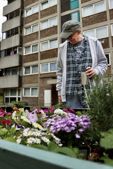 Man standing admiring flowers in front of a block of flats. Image by Abbey Wilkinson.