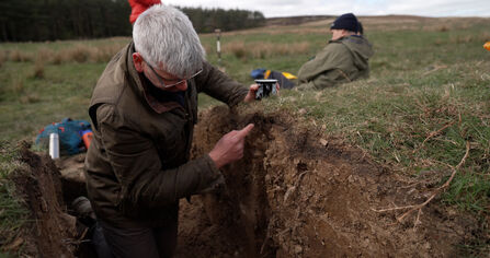 Dr Sam Turner from Newcastle University taking soil samples on The Rothbury Estate. He is stood in a trench taking samples 