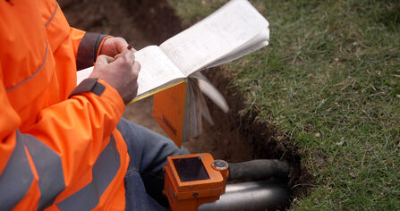 A person kneeling in a shallow pit making notes on a notepad. They are taking soil samples and dating it