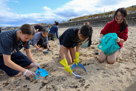 Young people kneeling in the sand and sifting for nurdles. Image by Leah Pattem.