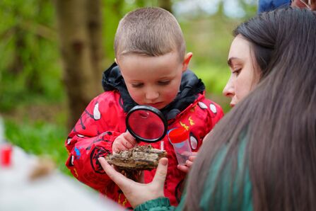 Young boy in a red coat looking through a magnifying glass. Image ALETC.