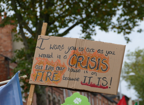 A poster at a climate march reads: "I want you to act as you would in a crisis. Act like our house is on fire because it is!"